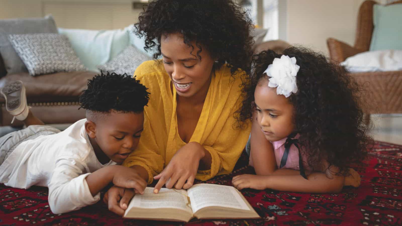 Front view of African American mother with her cute children lying on floor and reading a book.jpg