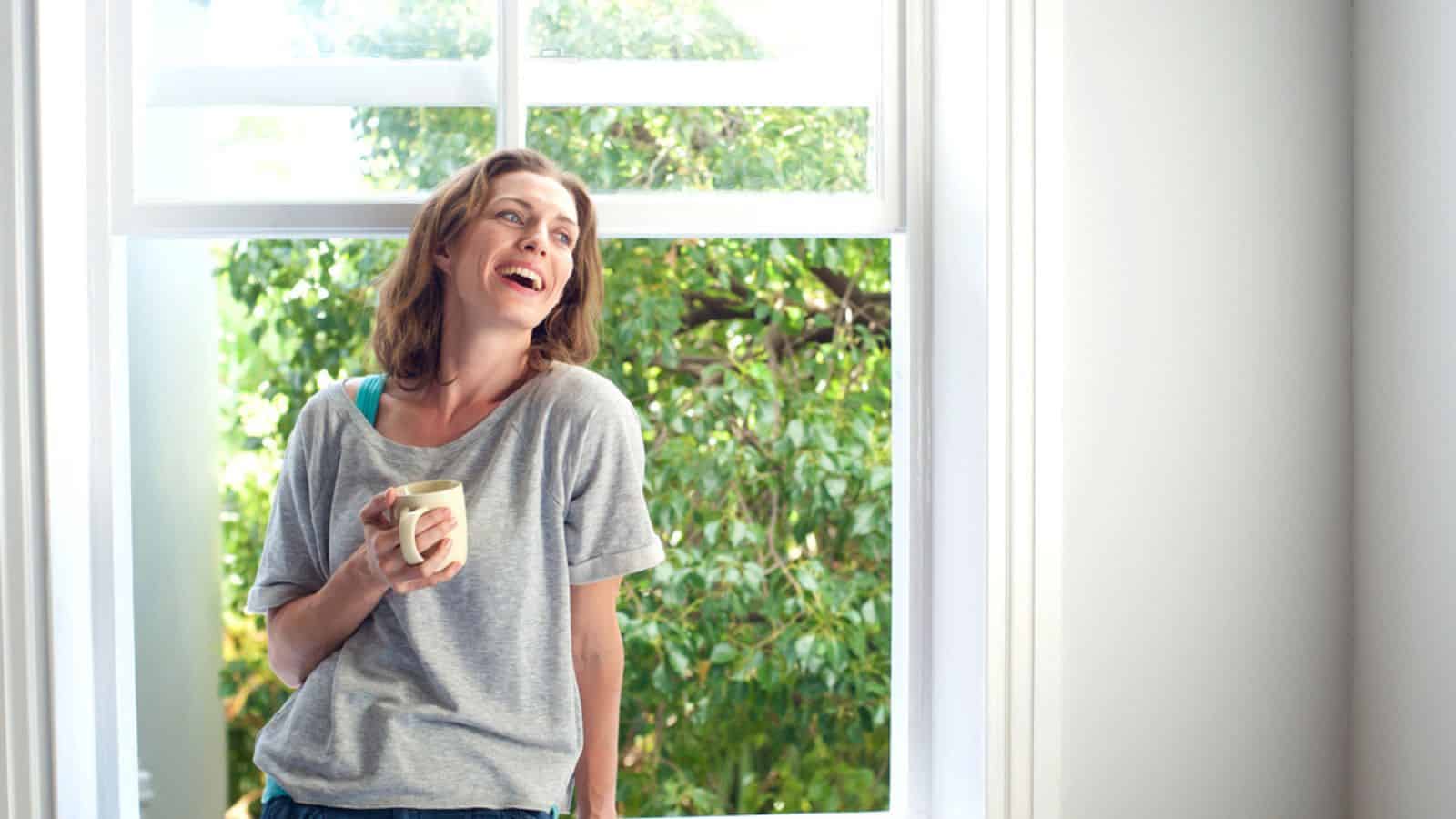 Happy woman laughing with a cup of coffee at home.jpg