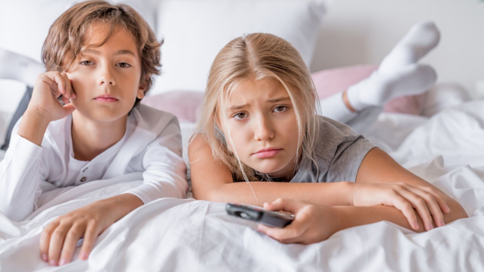 Boring boy and girl in pajamas lying in bedroom at home watching tv.jpg
